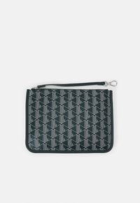 Pochette rectangulaire noire avec motif géométrique blanc et poignée détachable, accompagnée du texte « Lacoste » sur le tissu.