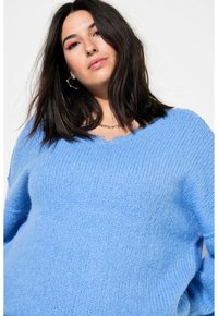 Pull en tricot bleu clair avec un col en V, tissu texturé et épaules tombantes. Le design présente une coupe ample et des détails côtelés subtils.