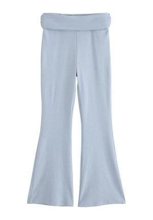 Ung person står iført en lyseblå hættetrøje og matchende vide bukser med hvide og beige sneakers mod en hvid baggrund.