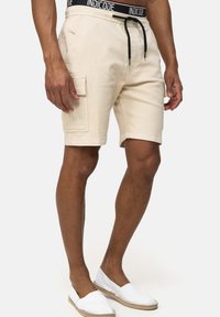 Beige cargo shorts med sidelommer, snøre i sort talje og en skræddersyet pasform. Glat bomuldsstof med synlige syninger.