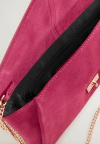 Pinkfarbene Schultertasche aus Wildleder mit einem goldfarbenen Kettenriemen, Reißverschluss und schwarzem Stofffutter. Auf der Vorderseite befindet sich ein rechteckiges Metallelement.