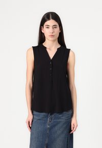 Blouse noire sans manches avec un décolleté en V, des boutons sur le devant et une texture lisse et légère. Associée à une jupe en denim.