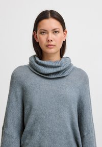 Maglione a collo alto di colore azzurro chiaro in morbido tessuto a maglia. Presenta una vestibilità ampia e un collo alto a costine. Tessuto con leggere variazioni nel filato.