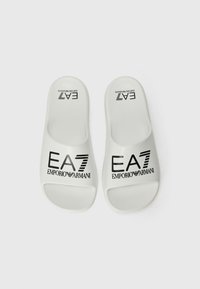 Bijele japanke napravljene od glatke plastike, s crnim logotipom s natpisom "EA7 EMPORIO ARMANI" otisnutim na gornjoj površini.