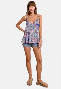Top peplum a fantasia multicolore con sottili spalline, caratterizzato da un design paisley blu, rosa e verde, abbinato a pantaloni shorts in denim.