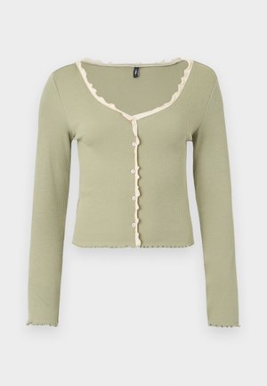 Φωτεινή πράσινη ριμπ πλεκτή ζακέτα με μακριά μανίκια και λευκή βολάν διακόσμηση κατά μήκος του λαιμού, της πατιλέτας με κουμπιά και των μανσετών, με κουμπιά στο εμπρός μέρος.