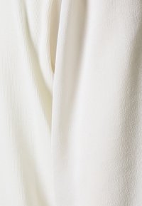 Vitt tyg med en texturerad yta och subtila ribbningar. Materialet ser mjukt och lätt ut, lämpligt för lager-på-lager.