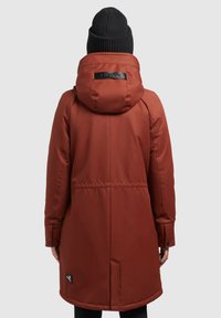 Rustrød parka med hætte, der har snoretræk, trykknapmansjetter og en sidelomme. Glat tekstur og minimalistisk design. Sort hue på modellen.