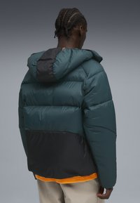 Padded jacket w kolorze teal i czarnym z kapturem. Posiada puchowy design, gładką fakturę oraz pomarańczowy akcent na dolnej krawędzi.