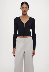 Navy kort cardigan med ribbet tekstur og lange ermer; har en dyp V-hals og en enkelt knappelukking foran.