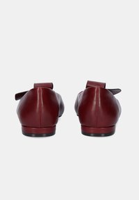 Zapatos de cuero burdeos con punta redondeada y un diseño elegante. Presentan una suela negra plana y un pequeño lazo decorativo en el talón.