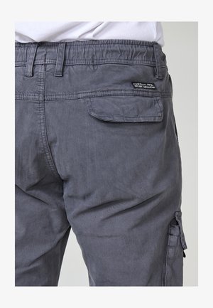 Szürke pamut cargo nadrág rugalmas derékkal, oldalsó zsebekkel és egy hátsó párna zsebbel. Finom texturált felülettel rendelkezik.