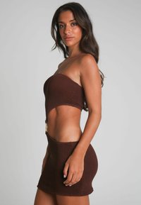 Ensemble crop top et mini-jupe en tricot marron avec un tissu texturé, présentant une découpe latérale et un accent en doré au niveau de la taille.