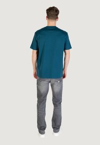 T-shirt in cotone color turchese con scollo rotondo e maniche corte, abbinata a jeans grigi. La t-shirt presenta una vestibilità comoda e un design semplice.