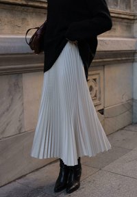 Hame pleated berwarna krem terbuat dari bahan lembut, dipadukan dengan sepatu bot pergelangan kaki hitam yang pas. Sweter terjuntai di atas rok, menambah kontras.