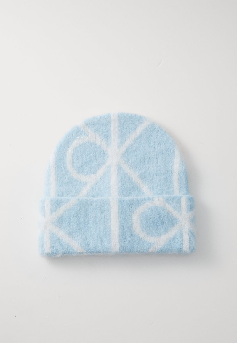 Bonnet en laine bleu clair avec un motif géométrique blanc, présentant un revers replié et une texture douce. Sommet arrondi sans coutures visibles.