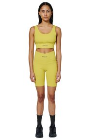 Gul crop top og cykelshorts sæt med "HALO" branding, glat tekstur, tætsiddende design, parret med sorte sneakers og sokker.