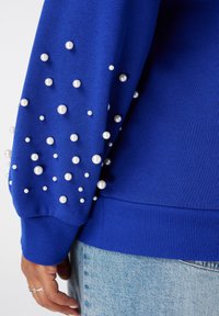 Blauwe sweatshirt met parelversieringen op de mouwen. Ribgebreide manchetten en zoom, zachte textuur, losse pasvorm en een uitgebreid patroon van variërende maatjes parels.