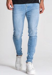 Jean skinny bleu clair en denim, avec une texture lisse et un léger délavage, associés à des baskets blanches.