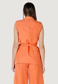 Top senza maniche in lino arancione con vita legata, caratterizzato da un sottile dettaglio sul retro e una vestibilità comoda, abbinato a pantaloni coordinati plissettati.