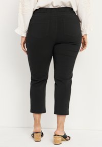 Zwarte cropped broeken met een elastische tailleband, achterzakken en een soepele textuur. Gepaard met zwart muiltjes met kurken hakken.