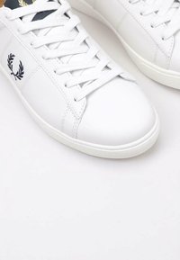 Sneaker in pelle bianca con lacci bianchi piatti, punta rotonda, branding blu sui lati e colletto imbottito per un maggiore comfort.