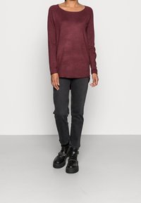 Haut bordeaux à manches longues avec un col rond, associé à un jean slim gris foncé et des bottines noires avec des accents de boucle.