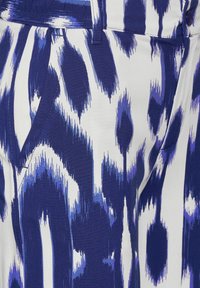 Mönstrad tyg med djärv blå och vit tiger-randig design, slät textur och synliga sömnads- och fickdetaljer.