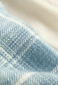 Blauw en wit geweven stof met een Houndstooth-patroon, dat een gestructureerd oppervlak en een zachte, gladde afwerking laat zien tegen een crèmekleurige achtergrond.