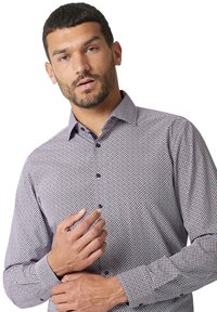 Heren overhemd met lange mouwen in een geometrisch patroon, met rode, blauwe en witte kleuren, een button-down kraag en contrasterende knopen.