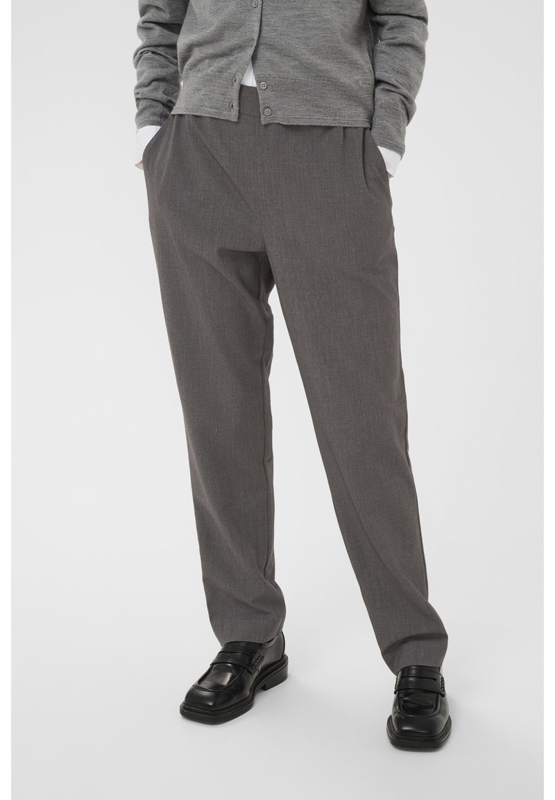 Grijze op maat gemaakte broeken met een lichte textuur, voorzien van plooien aan de voorkant en zijzakken, gecombineerd met zwarte schoenen en een grijze cardigan.