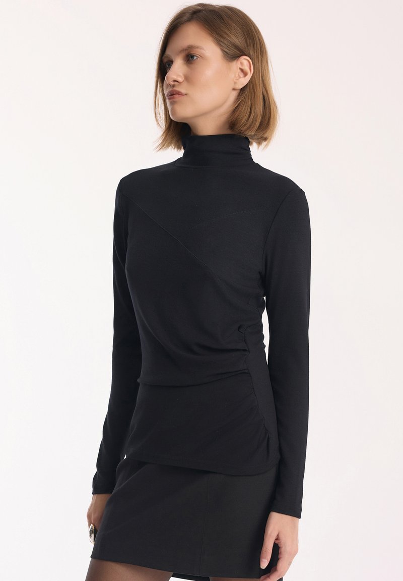 Czarny długi rękaw golf z ukośnymi szwami i marszczeniem po bokach, wykonany z miękkiego, elastycznego materiału dla dopasowanego wyglądu.