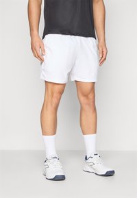 White athletic shorts with a smooth texture and an elastic waistband, paired with white socks and white athletic shoes with blue accents.