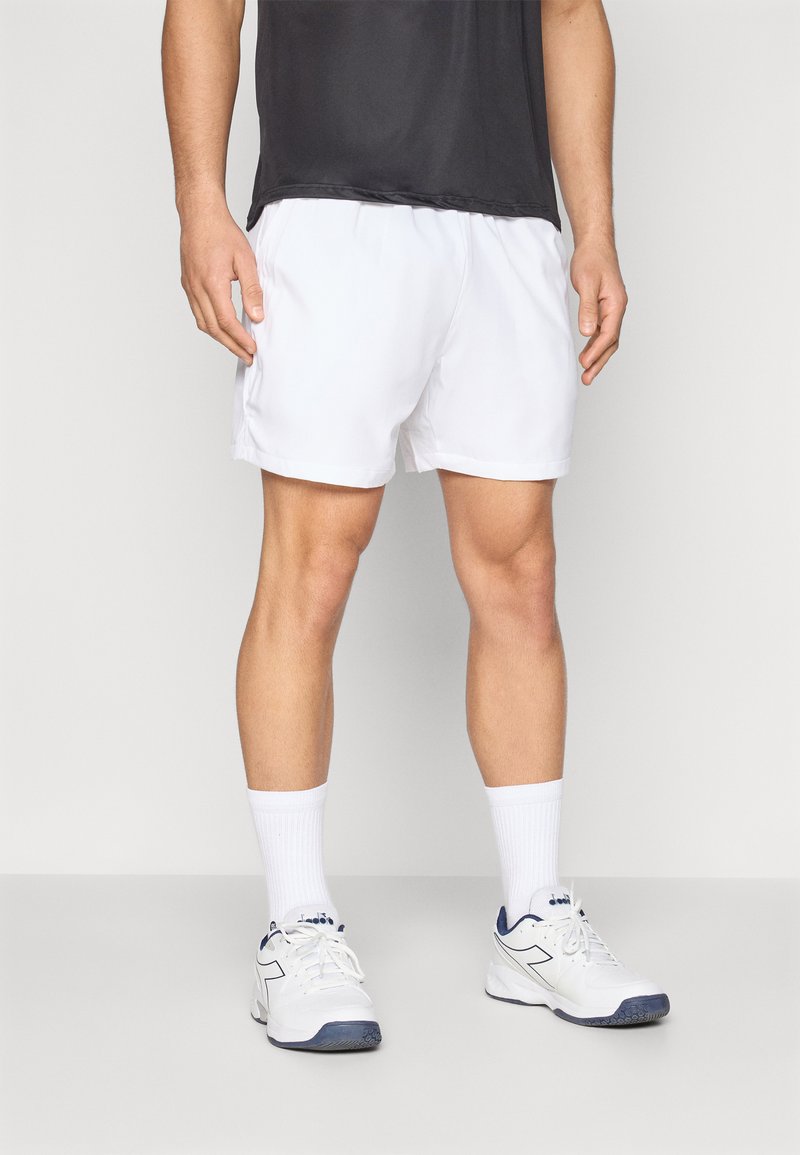 Pantalones cortos deportivos blancos con textura suave y cinturilla elástica, combinados con calcetines blancos y zapatillas deportivas blancas con detalles azules.