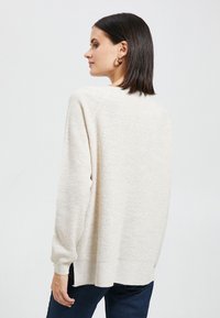 Beige gebreide trui met een relaxed fit, lange mouwen en zijsplitten. Zachte textuur en geribde manchetten, gestyled met donkere denim jeans.