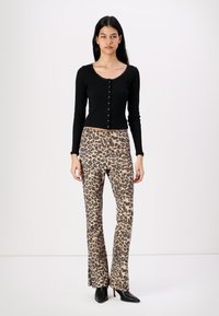 Crna rebrasta majica dugih rukava s kopčanjem sprijeda, uparena s trapericama leoparda s flared krojem. Outfit dopunjuju crne čizmice na petu.