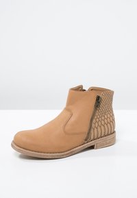 Vaaleanruskeat nilkkurit, jotka on valmistettu nahasta, sileällä etuosalla ja teksturoidulla käärmeennahkakuviolla takana. Sivussa vetoketjusuljenta ja tasapohja.