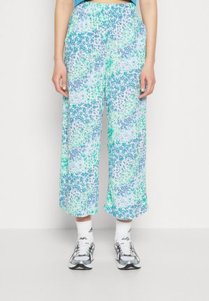 Pantalones sueltos y recortados con estampado floral en azul, verde y blanco, llevados con calcetines deportivos blancos y zapatillas de correr grises y blancas.