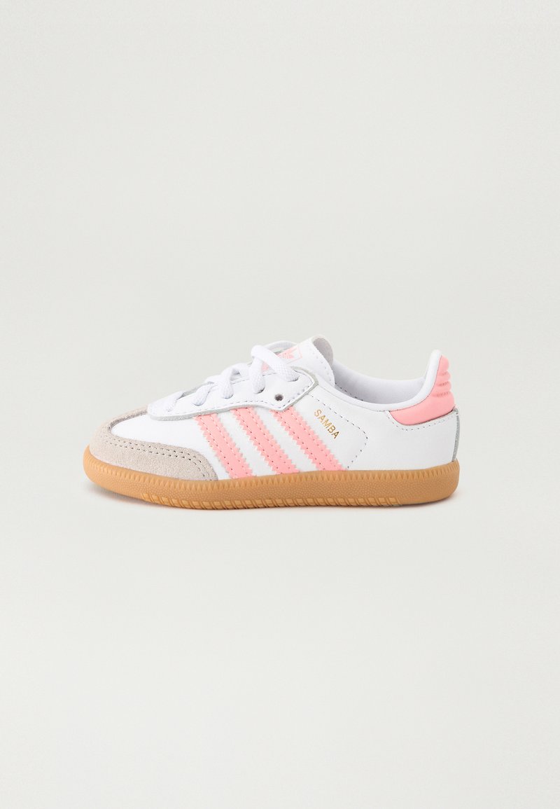 White retro sneakers with pink stripes, grey suede toe cap, and light pink heel accents. Textured gum rubber sole. Gold "Samba" branding.