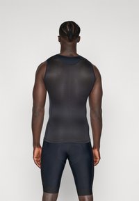 Schwarzes ärmelloses Sportoberteil mit passgenauer Passform und Netzstruktur, kombiniert mit schwarzen eng anliegenden Shorts, die über eine runde Nahtdetails verfügen.