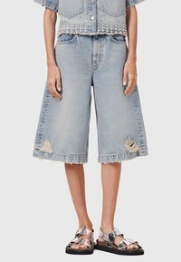 Culotte in denim azzurro chiaro con orli sfrangiati e dettagli strappati, abbinati a sandali metallici argentati. Tessuto testurizzato con vestibilità rilassata.