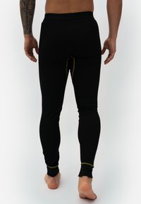 Black leggings made of stretchy fabric, featuring a fitted design, elastic waistband, and contrasting gold stitching along the seams.
