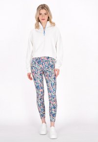 Pull bianco con zip a metà e tirante blu, abbinato a leggings aderenti con motivo multicolore e scarpe da ginnastica bianche.