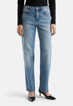 Jeans in denim blu con vestibilità dritta, cinque tasche, cuciture visibili e vita alta, abbinati a decolletè neri a punta.