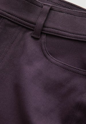 Dunkellila Stoff, der eine Nahaufnahme eines Taillenbunds zeigt, mit sichtbaren Nähten, einer kleinen Gürtelschlaufe und einem gewölbten Taschenöffnungsdetail.