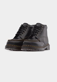 Ζευγάρι μαύρα δερμάτινα μποτάκια αστραγάλου με παχιά αυλακωτή σόλα, μεταλλικά κορδόνια και παχιά ραφή γύρω από την περιοχή των δακτύλων.