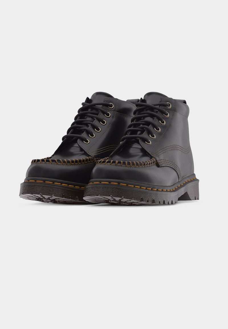 Een paar zwarte leren enkellaarsjes met dikke, gegroefde zolen, metalen veteroogjes en dikke stiksels rond het teengebied.