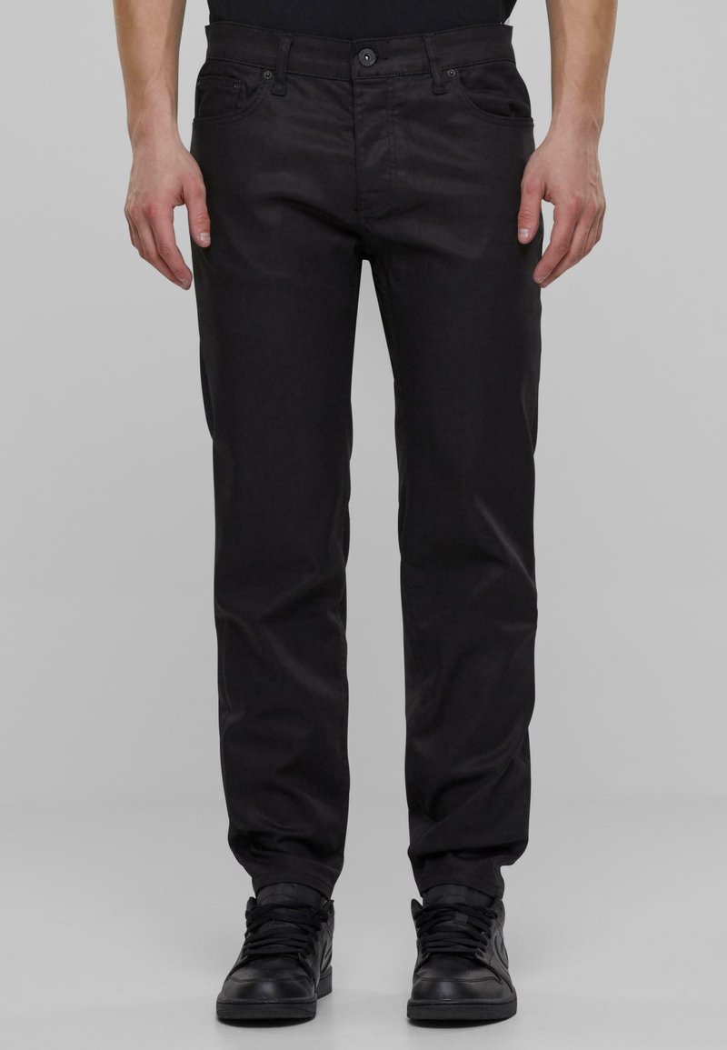 Pantalones casuales negros con un diseño de pierna recta, cinco bolsillos y un acabado de tela suave y ligeramente brillante. Combinados con zapatillas negras.