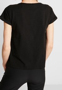 Sort bomulds T-shirt med opsmøgede ærmer, en afslappet pasform og rund halsudskæring. Glat tekstur, ingen synlige mønstre eller detaljer.