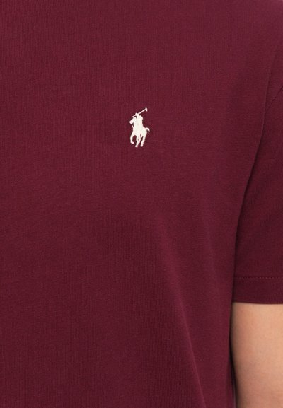Burgundijas kokvilnas T-krekls ar baltu izšūtu polo spēlētāja logotipu uz kreisā krūšu; gluda tekstūra un īsas piedurknes.